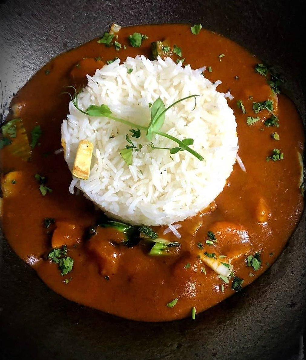 Caril alaranjado com uma cúpula de arroz branco e rebentos verdes por cima