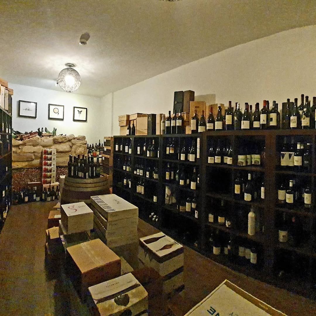 Garrafeira com estantes cheias de garrafas de vinho, caixas de madeira empilhadas e um barril